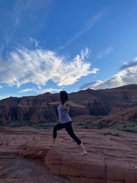 Dr. Sarah-Anne Schumann in warrior pose under a blue sky in Utah.